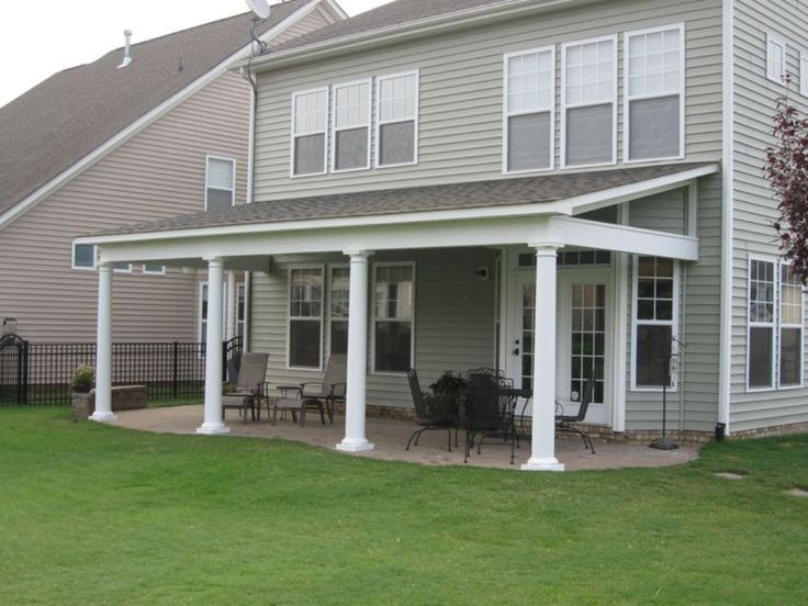 Covered back patio with white columns and outdoor furniture attached to a two-story home with a green lawn.