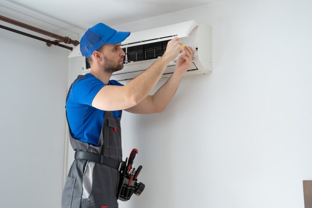 Technician in blue and grey uniform repairing a wall-mounted air conditioner.