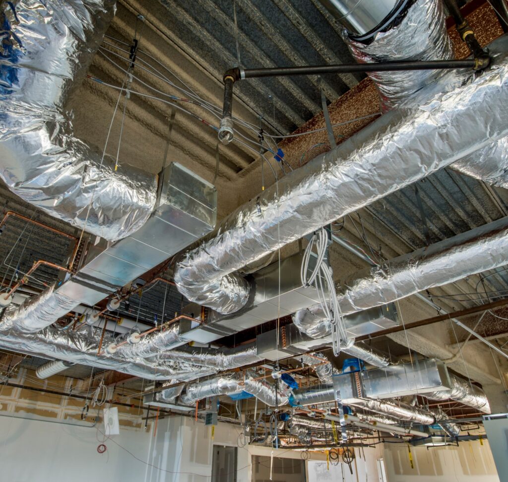 Exposed industrial ceiling with foil-wrapped HVAC ductwork, copper piping, and electrical conduits.