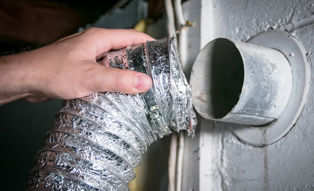 A hand connecting a flexible aluminum vent duct to a rigid wall pipe.