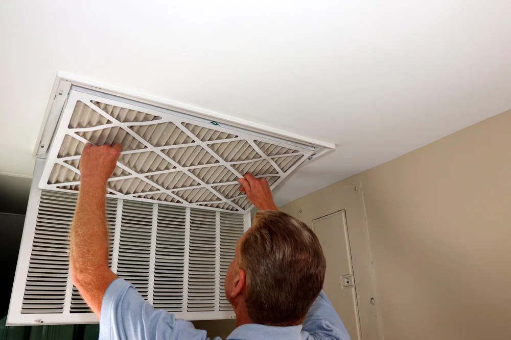 A man replacing a ceiling air filter in an HVAC unit.
