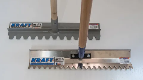 Two Kraft concrete placer rakes with wooden handles, one with a gray head and one with a stainless steel head.