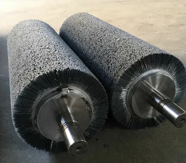 Two industrial cylindrical roller brushes with dense abrasive wire bristles and steel shafts.