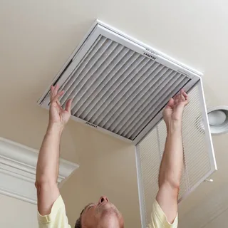 Person replacing a pleated HVAC air filter in a ceiling vent.