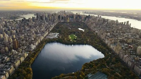Aerial view of Central Park and its reservoir surrounded by New York City skyscrapers during a golden sunset.