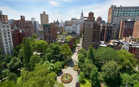 Aerial view of a lush green city park surrounded by a dense skyline of tall brick and stone buildings.