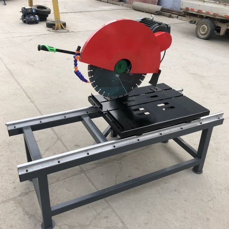 Industrial stone and tile saw with a red blade guard, diamond blade, and sliding table on a steel frame.