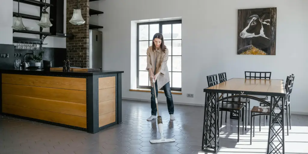 Woman mopping a gray tiled floor in a modern open-concept kitchen and dining area.