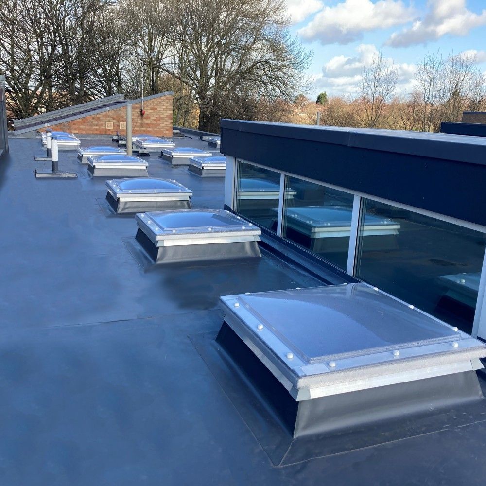 Flat grey waterproof roof with multiple square skylights and a raised clerestory window section.