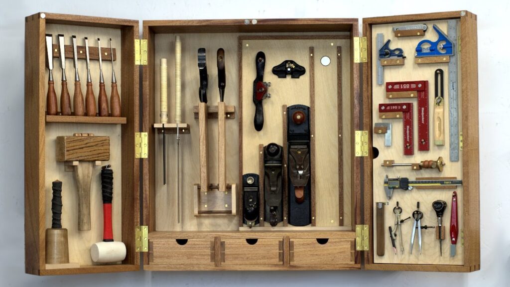 Open wooden tool cabinet displaying neatly organized hand tools including chisels, mallets, hand planes, and squares.