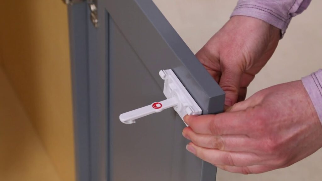 Hands attaching a white plastic magnetic cabinet catch to the edge of a grey cabinet door.