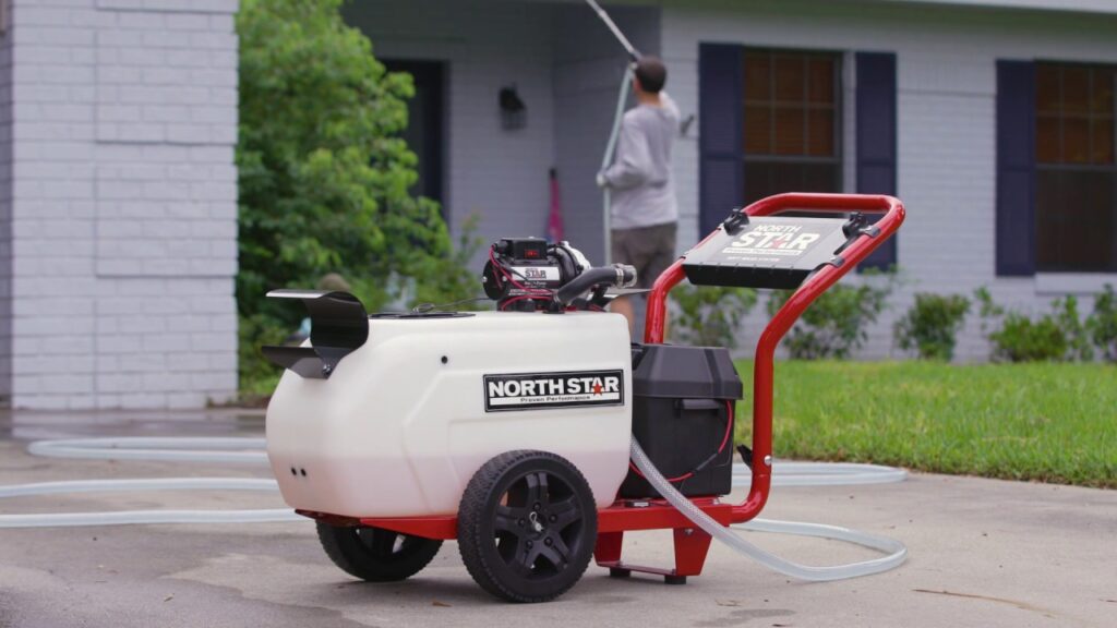 North Star soft wash system with white tank and red frame on a driveway, with a person using a sprayer in the background.