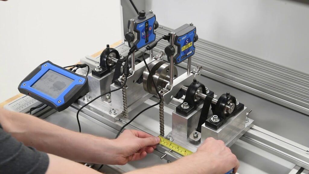 Hands using a yellow tape measure on a mechanical test rig with SKF sensors and a digital display.