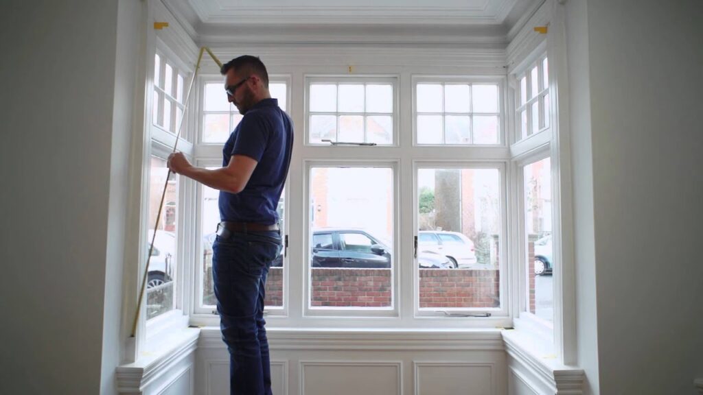 Man measuring a white bay window with a measuring tape.