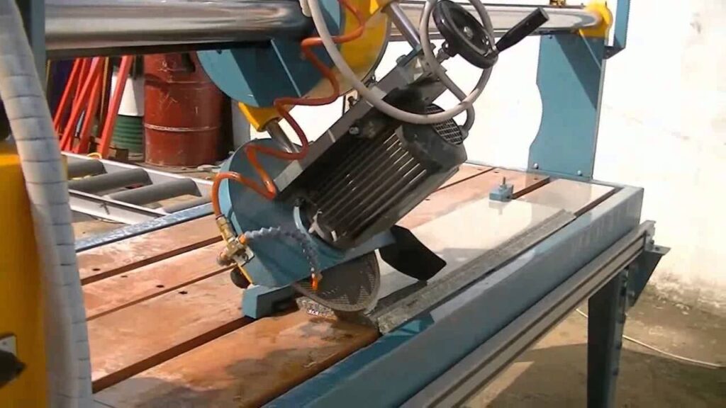 Industrial bridge saw with a diamond blade cutting a stone slab on a metal work table.