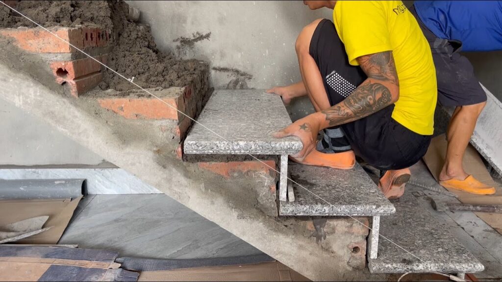 Worker installing granite slabs on a concrete staircase using a string line for alignment.