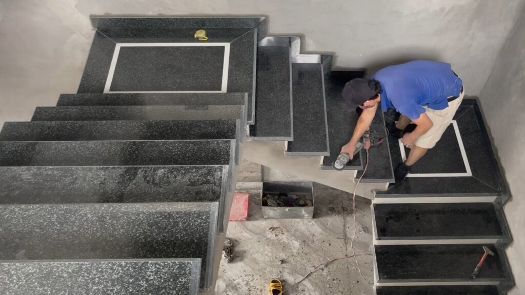 A worker uses a hand grinder to polish black granite steps during staircase installation.