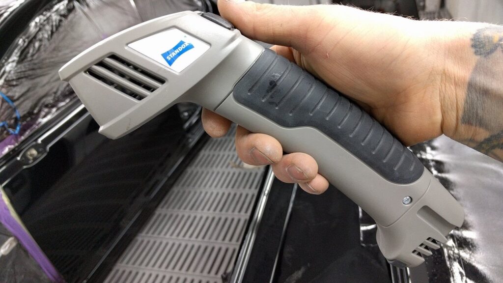 Hand holding a grey and black Standox color matching scanner.