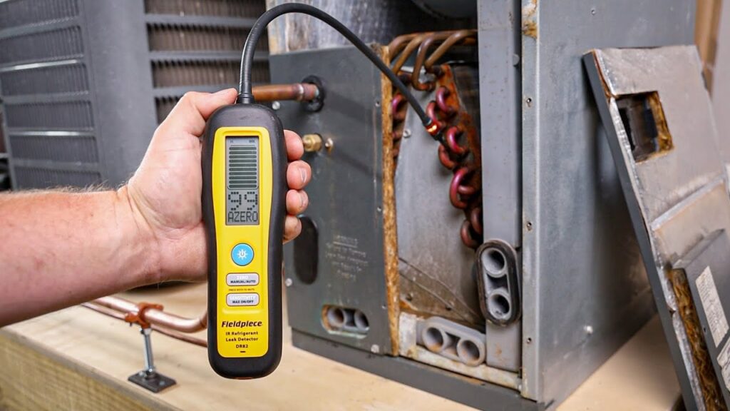 Hand using a yellow Fieldpiece DR82 refrigerant leak detector to check an HVAC unit.