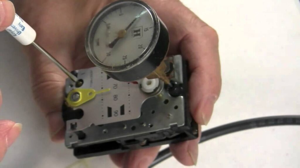 A hand using a small tool to adjust a metal valve assembly with an attached pressure gauge.