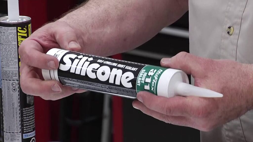 Hands holding a tube of Nuflex 311 self-levelling silicone joint sealant.