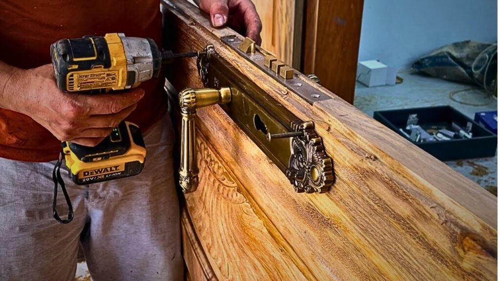 Person using a power drill to install an ornate brass handle and lock onto a carved wooden door.