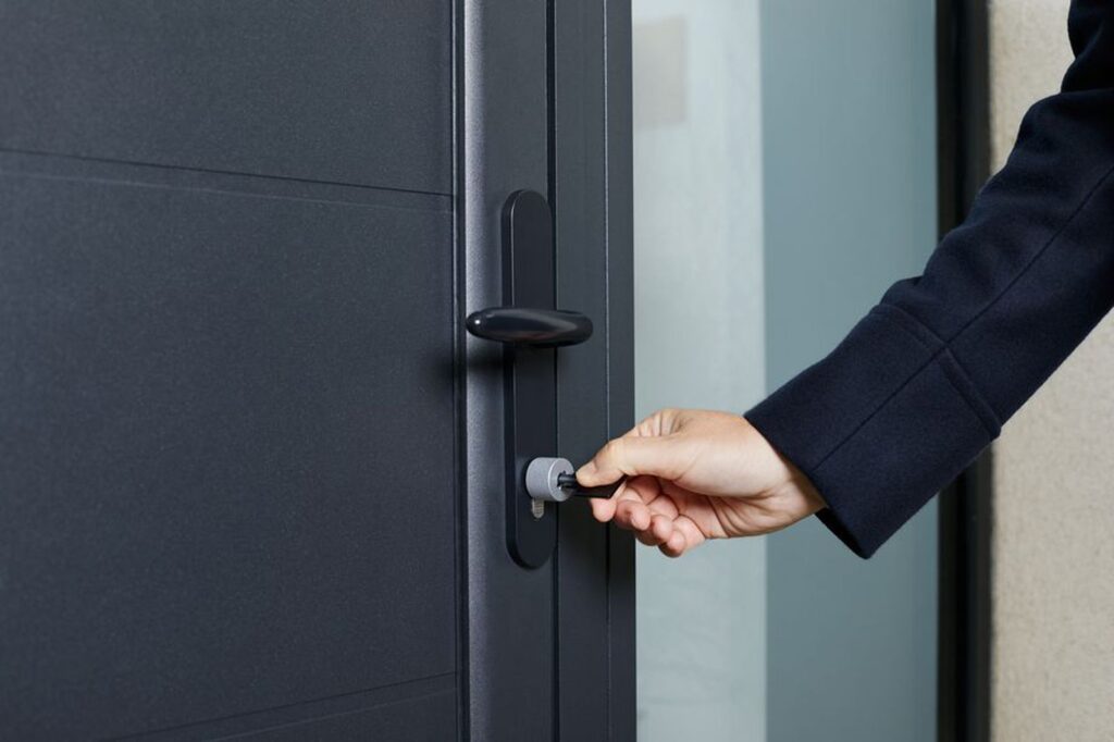 A hand inserting a key into the lock of a modern dark grey door.