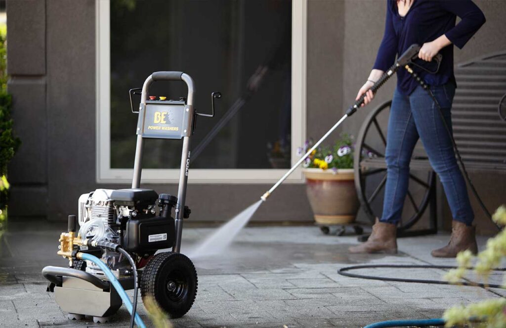 A woman using a BE gas-powered pressure washer to clean a stone patio.