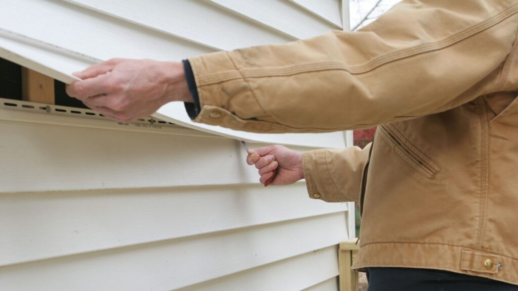 Person using a utility knife to cut white vinyl siding on a house.