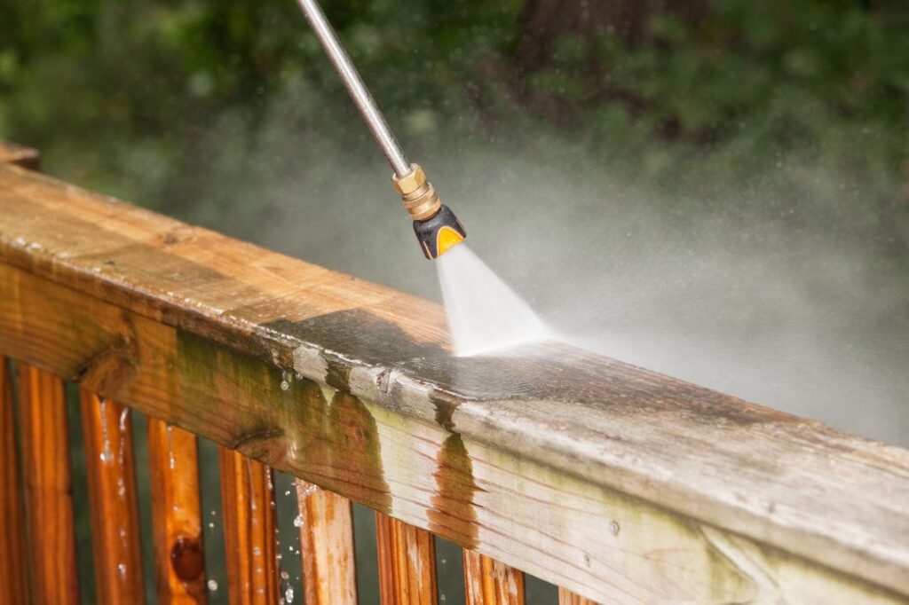 High-pressure water spray cleaning a weathered wooden deck railing.