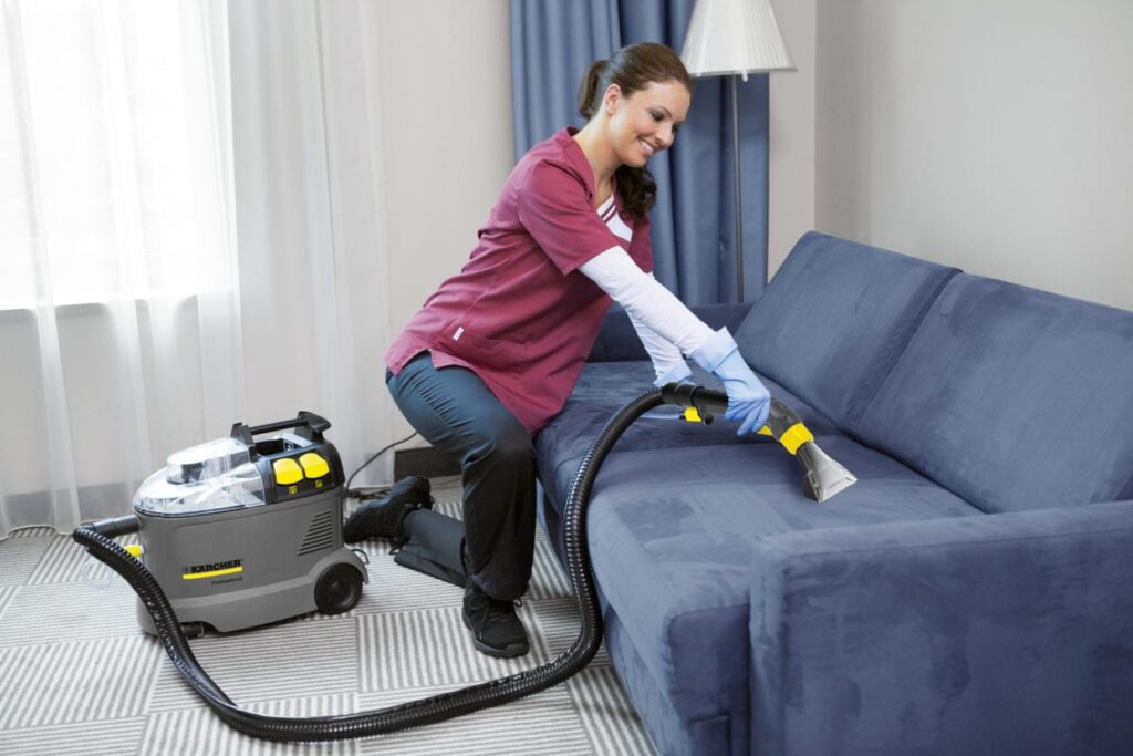 A cleaning professional using a Karcher spray-extraction cleaner to deep clean a blue fabric sofa.