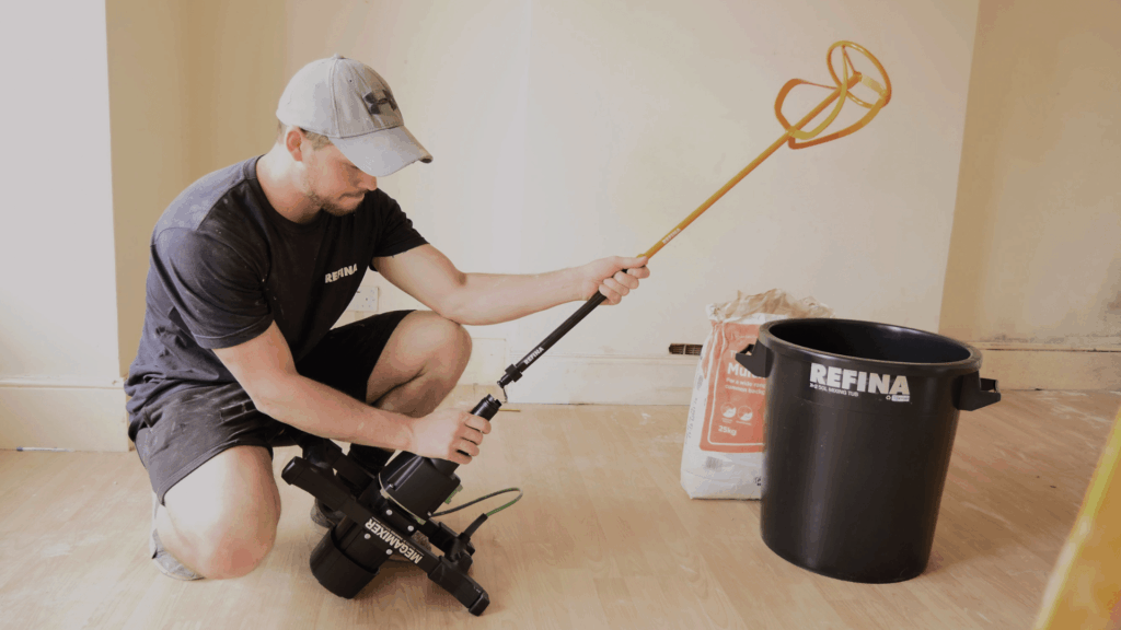 Man assembling a Refina Megamixer and paddle next to a black mixing bucket on a wooden floor.
