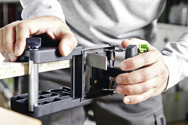 Hands operating a black woodworking jig on a piece of light-colored wood.