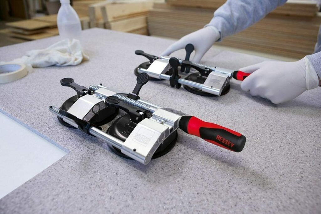 Worker using Bessey suction cup seam setters to align two pieces of a gray countertop.