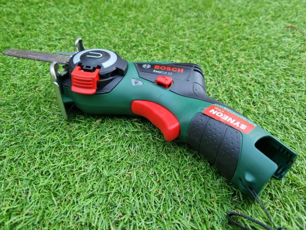 Green and red Bosch EasyCut 12 cordless power saw resting on green artificial grass.