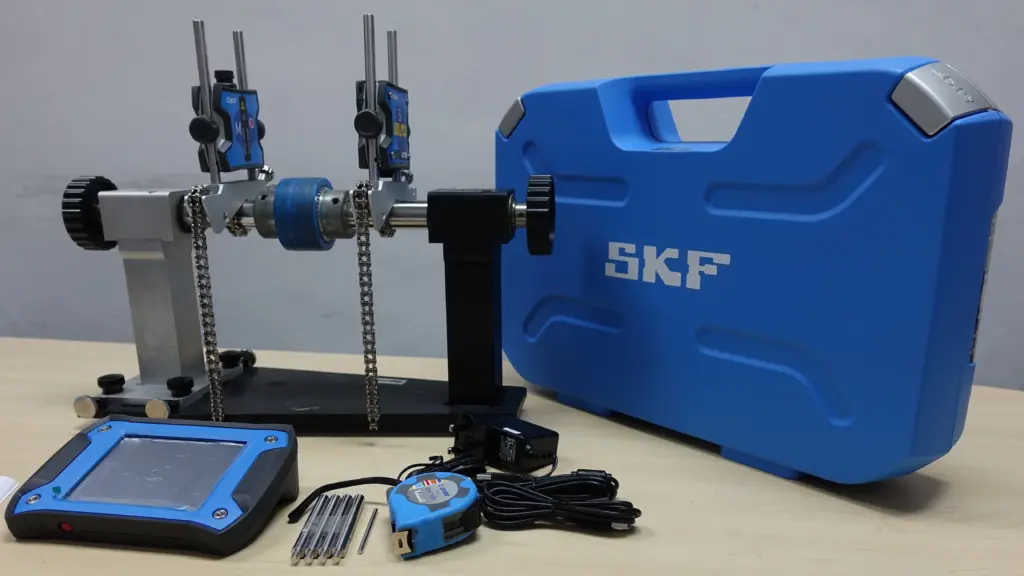 SKF laser shaft alignment kit with display tablet, measuring sensors on a shaft rig, and a blue carrying case.