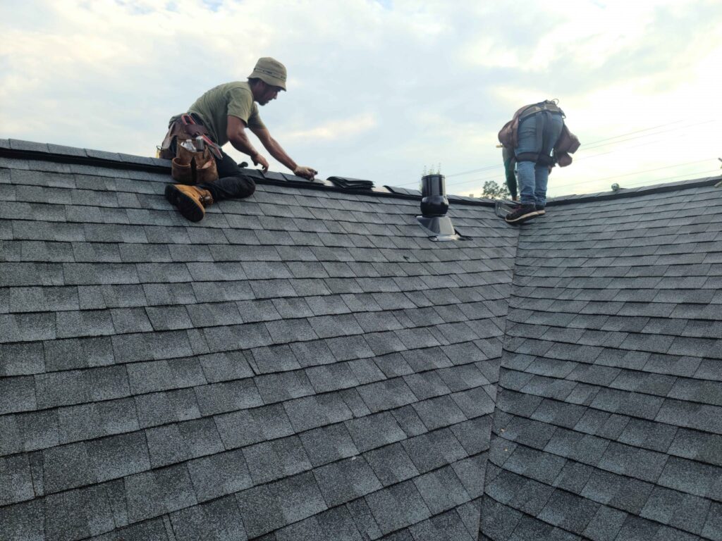 Two roofers installing grey asphalt shingles on a residential roof.