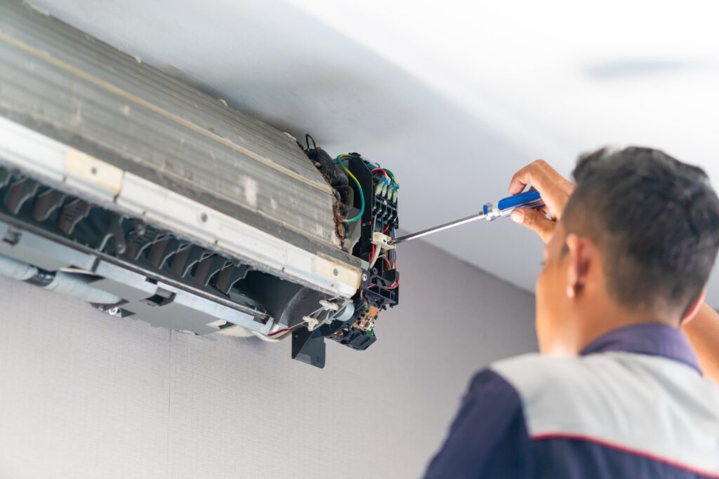 Technician repairing a wall-mounted air conditioning unit with a screwdriver.
