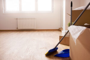 Empty room with light wood floors, moving boxes, and a blue broom and dustpan.