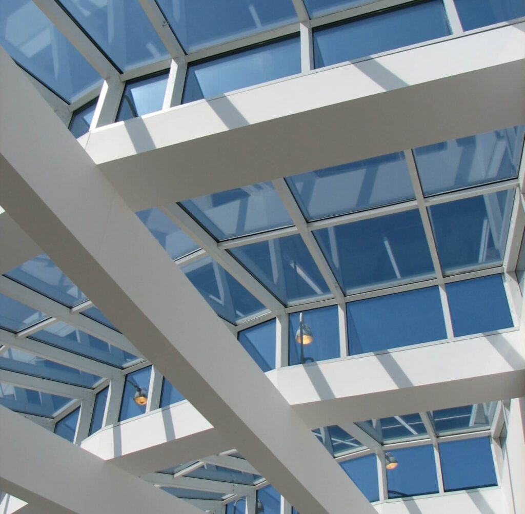 Low-angle view of a modern white architectural structure with glass ceiling panels and a clear blue sky.