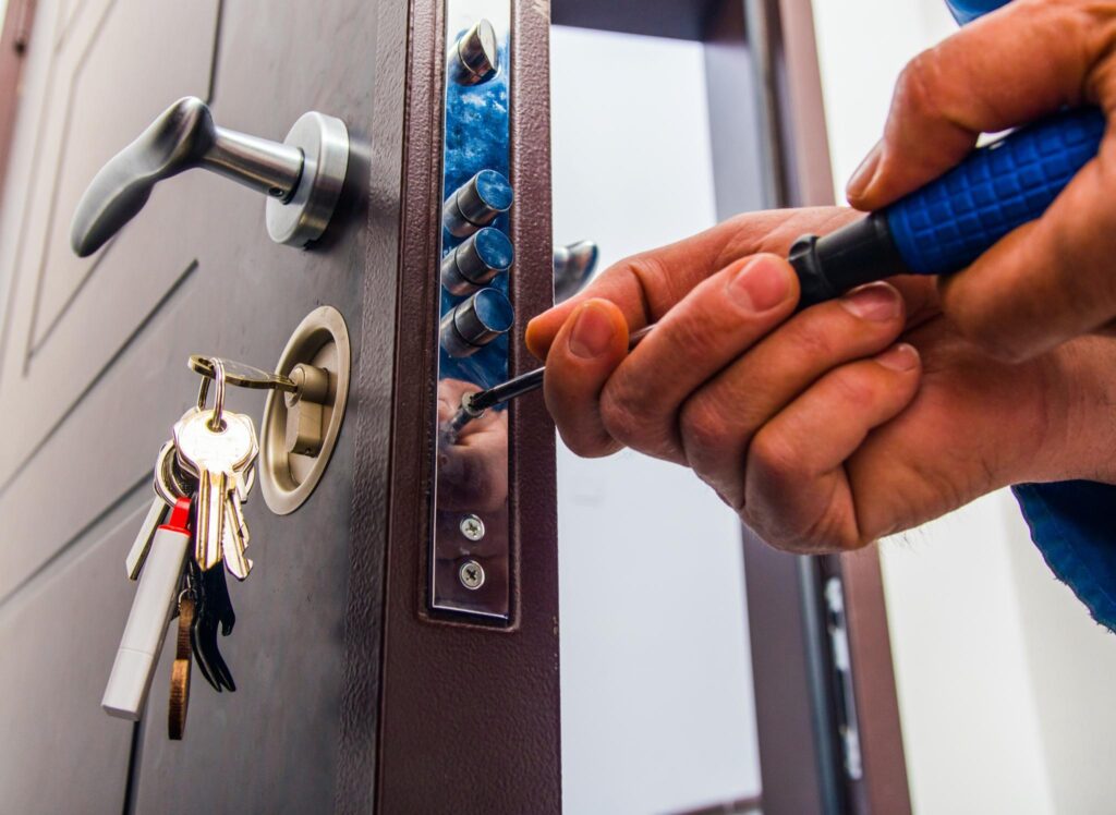A person using a screwdriver to install or repair a metal lock mechanism on a brown door.