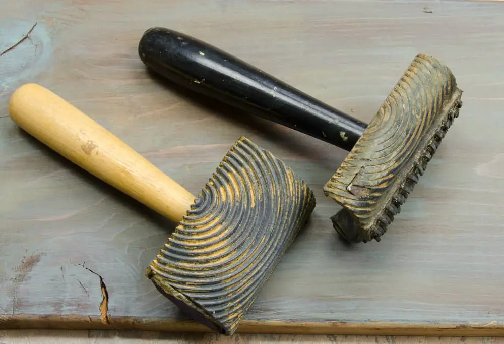 Two textured hand tools with ribbed heads and wooden handles on a grey weathered wooden surface.