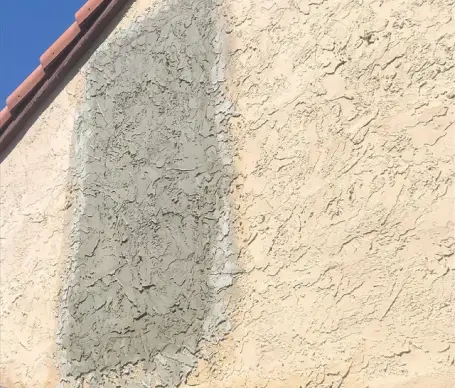 Grey stucco repair patch on a beige textured exterior wall.