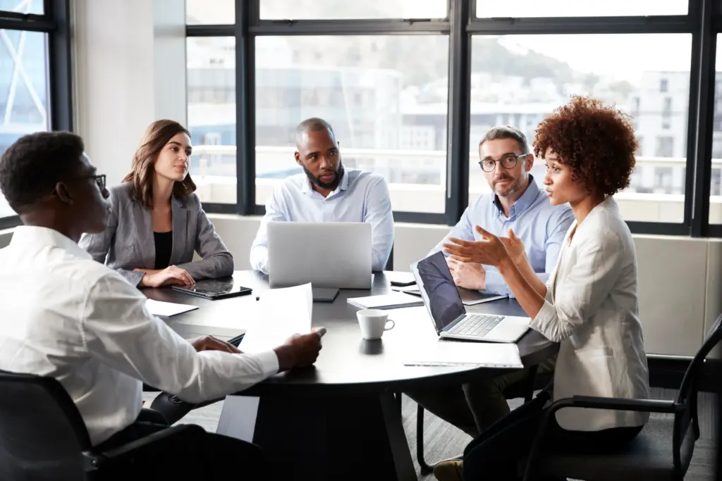 Diverse business colleagues listening to a colleague speak during a meeting at a conference room table.