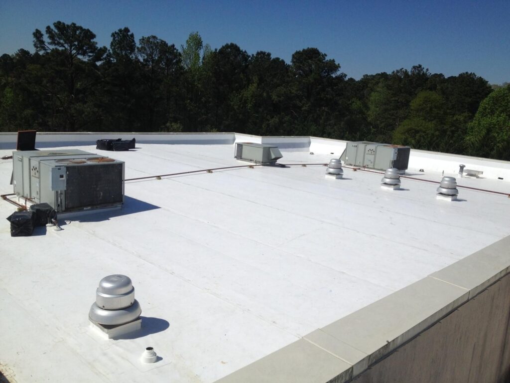 Flat white commercial rooftop featuring HVAC air conditioning units and exhaust vents surrounded by trees.
