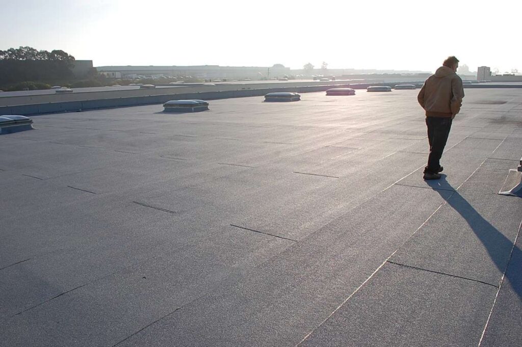 A person stands on a flat, expansive commercial rooftop under bright, hazy sunlight.