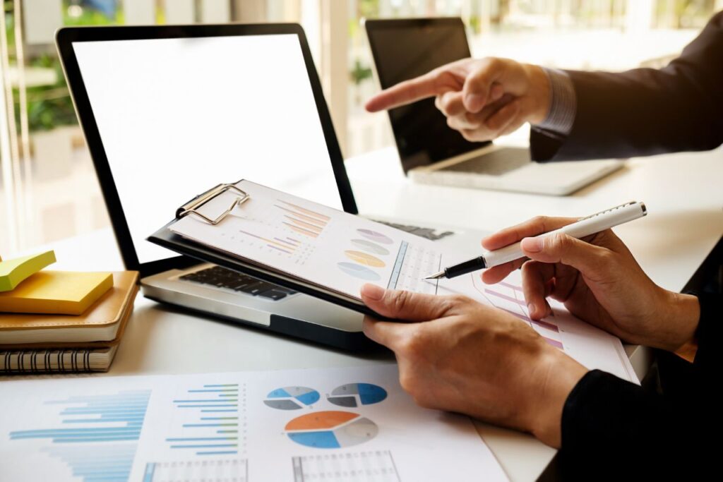 Colleagues reviewing printed financial charts and graphs on a clipboard in front of a laptop.