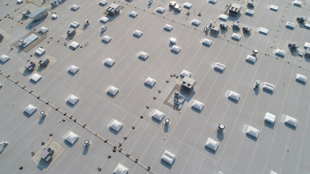 Aerial view of a grey commercial flat roof dotted with white skylights and HVAC ventilation systems.