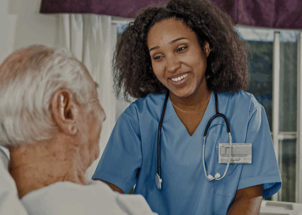 Smiling nurse in blue scrubs with a stethoscope interacting with an elderly patient.