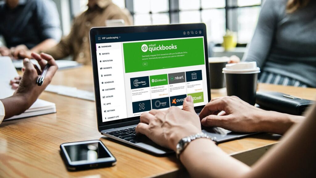 Hands typing on a laptop displaying the Intuit QuickBooks dashboard during a business meeting.